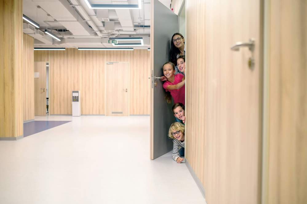 Des élèves joyeux et leur éducatrice ouvrent une porte donnant sur un couloir vide