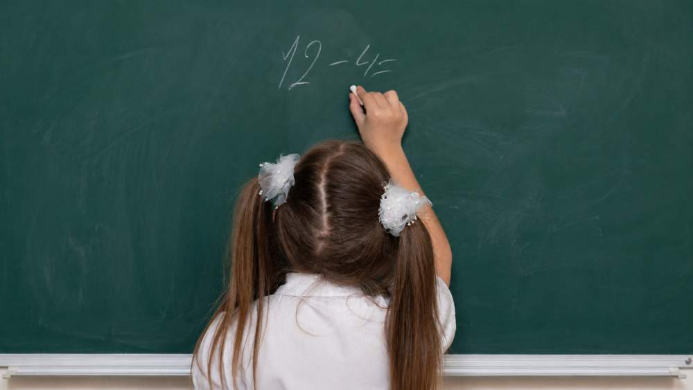 Petite fille écrivant au tableau "12-4"