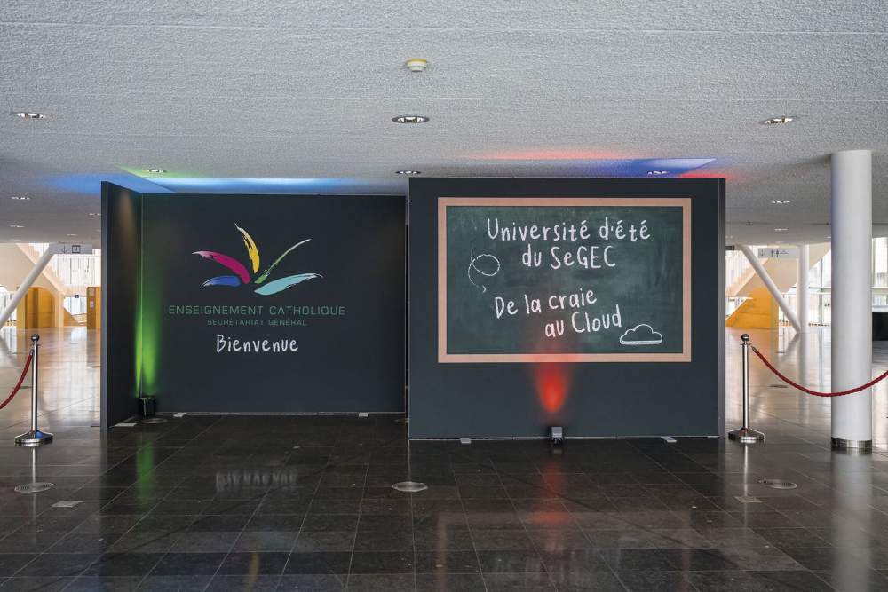 Une toile noire où est accroché un tableau avec la mention "Université d'été du SeGEC : de la craie au cloud"
